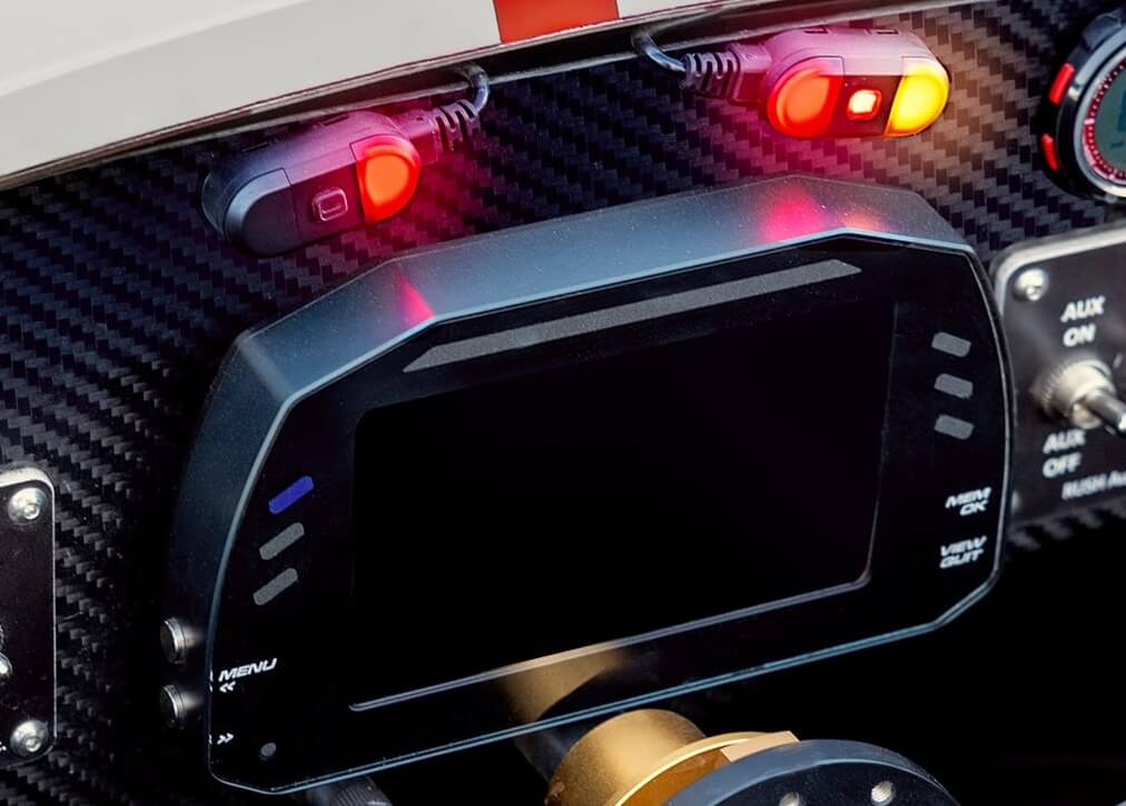 Car dashboard with a central touchscreen display on a carbon-fiber panel and red indicator lights above.